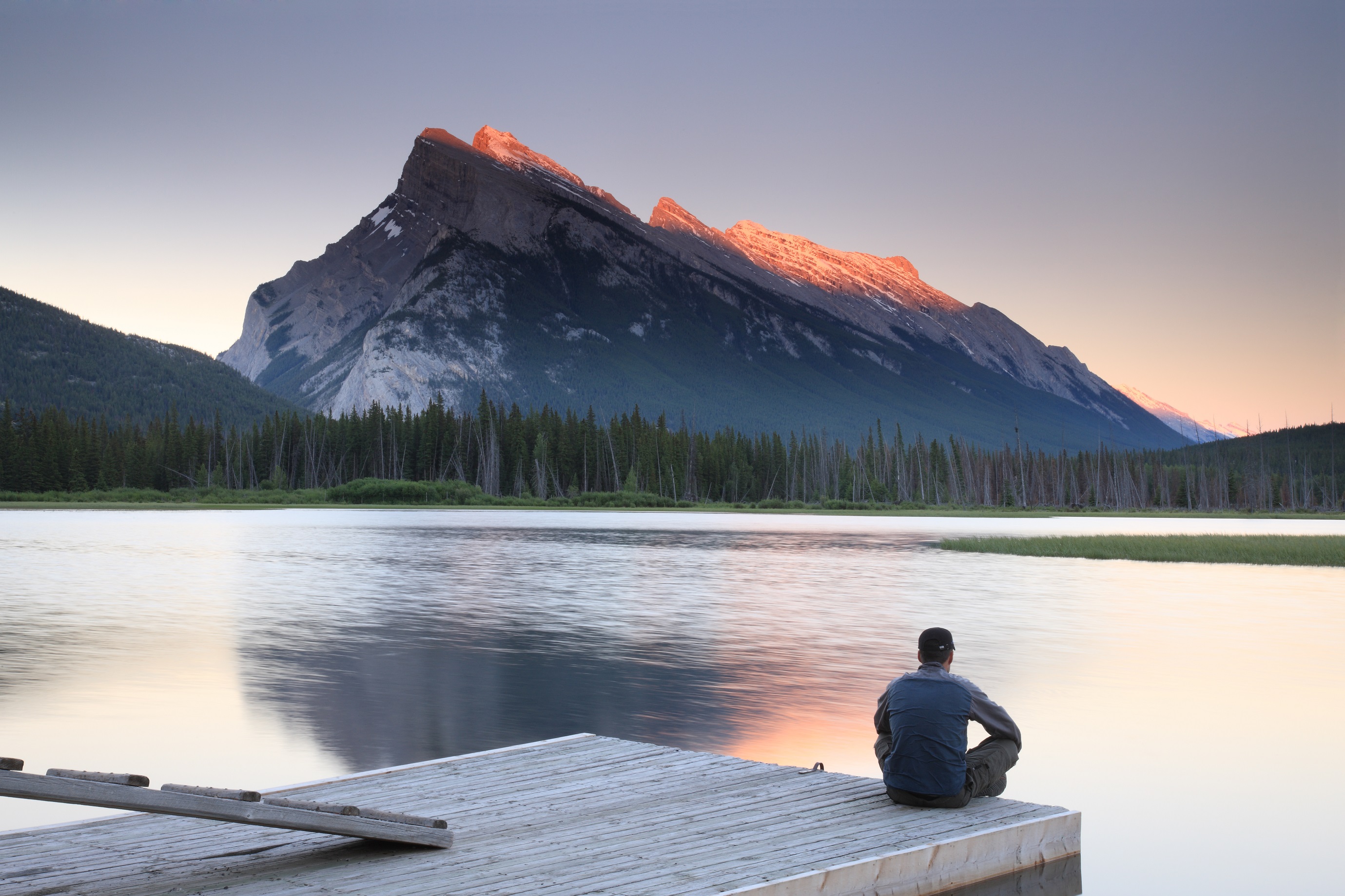 Man sitting on edge of dock by Mount Rundle, Banff