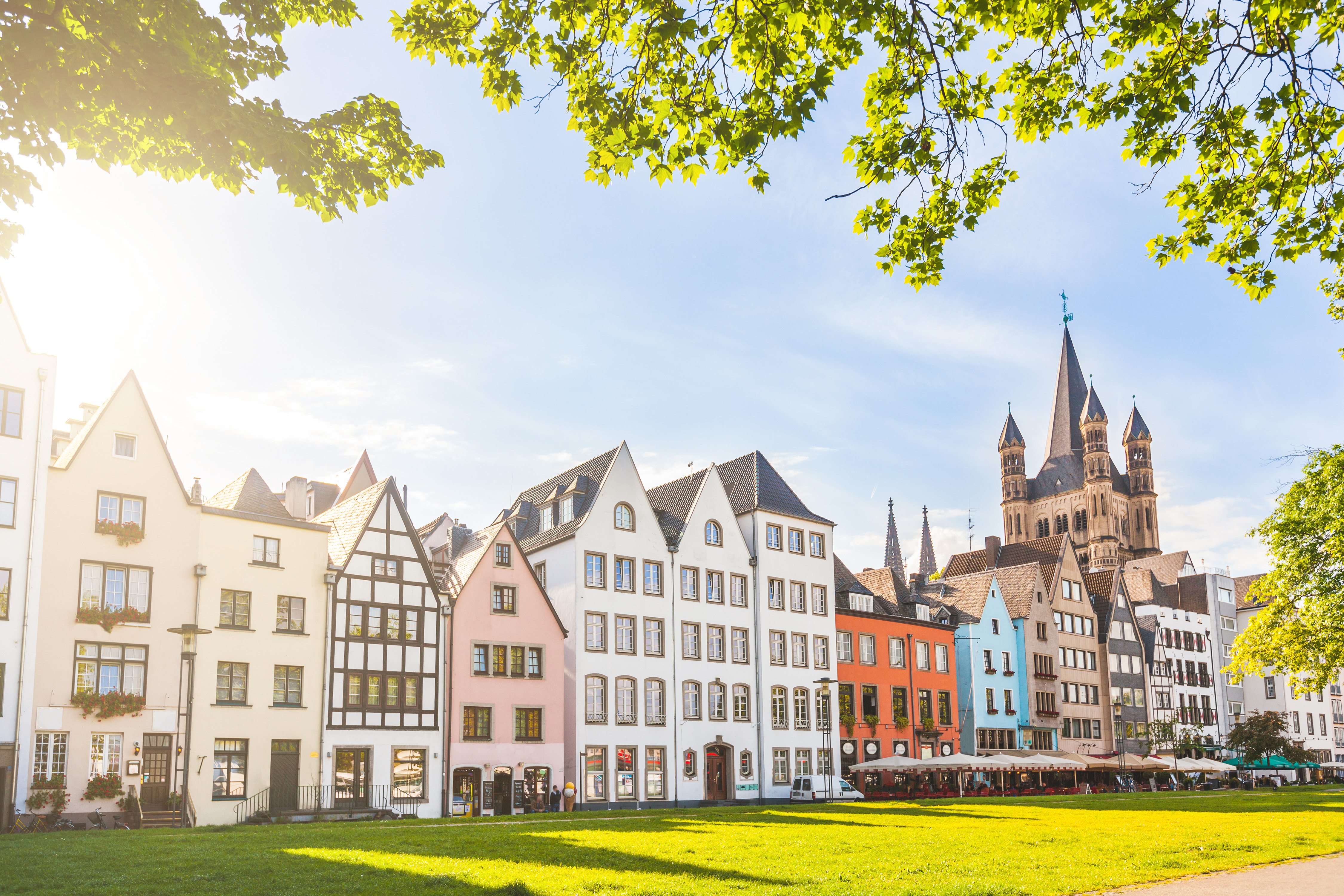 Houses and park in Cologne, Germany. Many of them are colourful, they are facing a public park with green grass and some trees. There is a bell tower on background. Travel and architecture concepts.